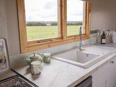 A kitchen countertop with a sink teapot two mugs and wine glasses near windows at Shepherds Hut in Garthorpe near Scunthorpe