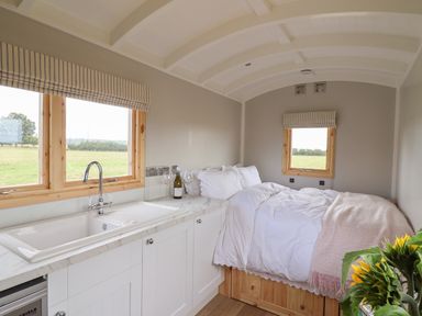 A small room with a kitchen sink and cabinets next to a bed with white bedding and a blanket at Shepherds Hut in Garthorpe near Scunthorpe