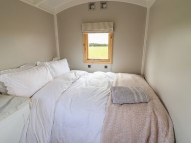 A bedroom with a bed covered in white bedding and a folded towel on a blanket near a window at Shepherds Hut in Garthorpe near Scunthorpe