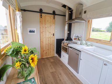 A kitchen with a wooden sliding door a bouquet of sunflowers on a wooden table a stove a small refrigerator and a sink at Shepherds Hut in Garthorpe near Scunthorpe