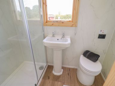 A bathroom with a shower enclosure a pedestal sink and a toilet with a towel on it at Shepherds Hut in Garthorpe near Scunthorpe