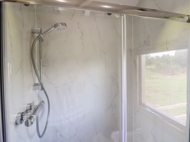 A shower area with a handheld showerhead and glass door with a window showing outdoor scenery at Shepherds Hut in Garthorpe near Scunthorpe