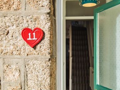 A stone wall with a red heart-shaped house number 11 and an open door showing a hallway with stairs at 11 Belgravia Street in Penzance