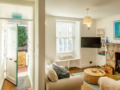 A living room with a beige sofa a round wooden coffee table a wall mounted TV and a stone fireplace at 11 Belgravia Street in Penzance