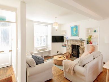 A living room with two sofas a round coffee table a stone fireplace and a wall-mounted television at 11 Belgravia Street in Penzance