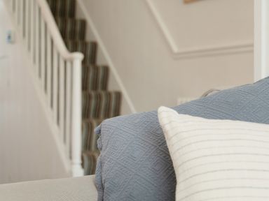 A close up of a couch with a blue throw and white pillow in front of a staircase with striped carpet at 11 Belgravia Street in Penzance