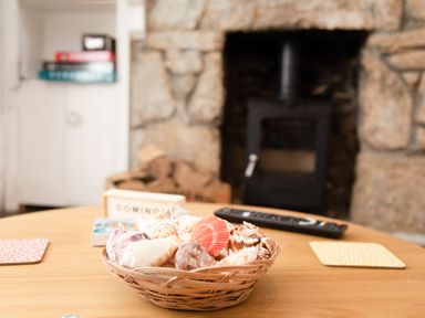 A basket of seashells on a wooden table with a remote control and cosy fireplace in the background at 11 Belgravia Street in Penzance