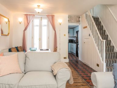 A living room with a beige sofa striped pillows and a dining table near glass doors at 11 Belgravia Street in Penzance