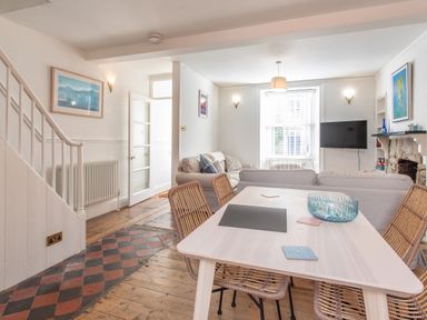 A dining table with four wicker chairs and a living room with sofas a TV and artwork at 11 Belgravia Street Penzance