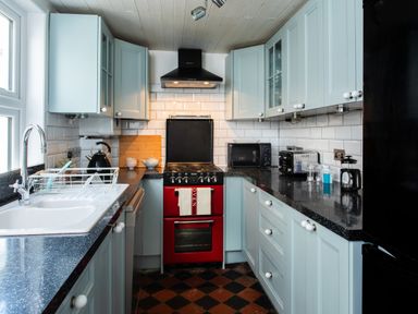 A kitchen with blue cabinets a red oven a black microwave and a white sink at 11 Belgravia Street in Penzance