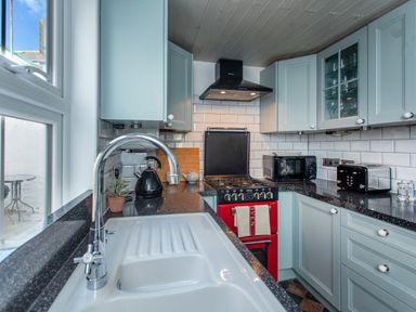 A kitchen with a white sink and chrome faucet light blue cabinets black countertop a red oven a black microwave and a black toaster at 11 Belgravia Street in Penzance
