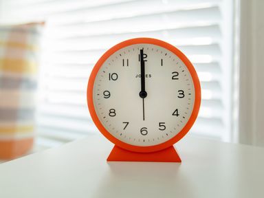 A round orange clock showing twelve o'clock on a white surface with window blinds in the background at 11 Belgravia Street in Penzance