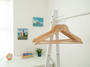 A white room with wooden hangers on a white freestanding rack and a table with books plant and clock at 11 Belgravia Street in Penzance