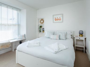A bedroom with a white bed and striped pillows near a window with blinds at 11 Belgravia Street in Penzance