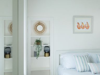 A bedroom with a bed and striped pillows a framed artwork of shrimps and a built-in shelf with a plant and a lamp at 11 Belgravia Street in Penzance