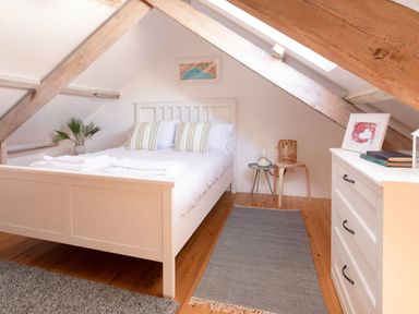 A bedroom with a white bed, pillows, a plant, bedside tables, a rug, and a white dresser at 11 Belgravia Street in Penzance