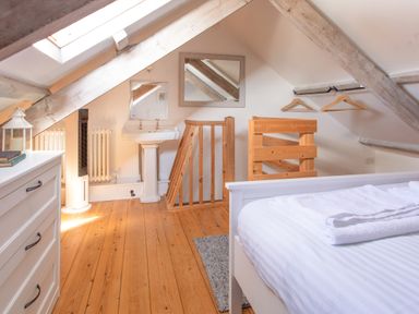 An attic bedroom with a bed a white dresser a wooden railing a small sink two mirrors and clothes hangers at 11 Belgravia Street in Penzance