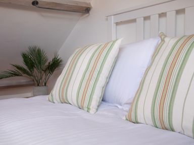A bed with striped pillows and white sheets near a plant at 11 Belgravia Street in Penzance
