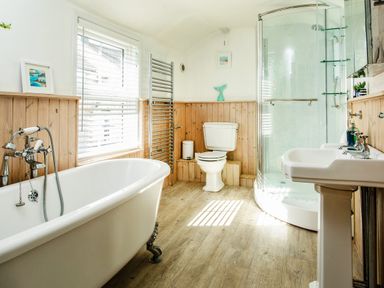 A bathroom with a freestanding bathtub a window with blinds a toilet a glass shower enclosure and a pedestal sink at 11 Belgravia Street in Penzance