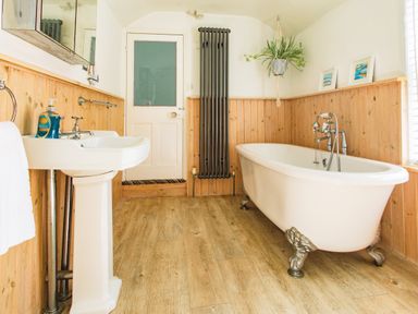 A bathroom with a white freestanding bathtub and a pedestal sink with wooden paneling on the walls at 11 Belgravia Street in Penzance
