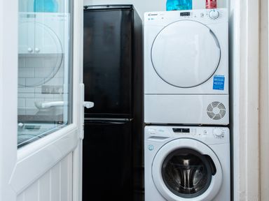 A laundry area with a stacked white washer and dryer and a black refrigerator at 11 Belgravia Street in Penzance