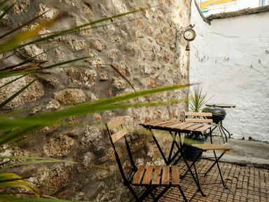 A small outdoor patio with two wooden chairs a wooden table a potted plant a wall clock and a barbecue grill at 11 Belgravia Street in Penzance