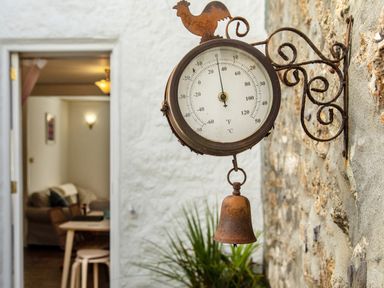 A rusted outdoor thermometer with a bell mounted on a stone wall outside a doorway at 11 Belgravia Street in Penzance