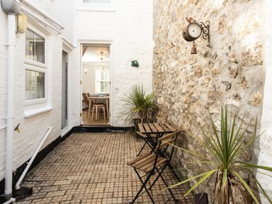 An outdoor patio with a small wooden table and two chairs next to a stone wall with plants and a vintage clock at 11 Belgravia Street in Penzance
