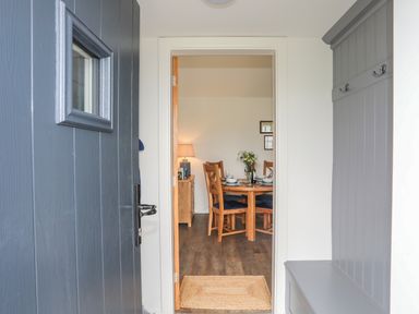 Entryway with a blue door and gray bench with hooks leading to a dining area with a wooden table and chairs at Bwthyn Y Swnt in Moelfre