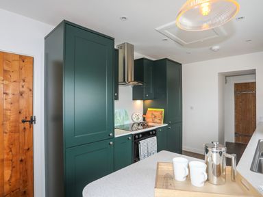 A kitchen with green cabinets a stove wooden doors and a tray with a coffee pot and cups on a counter at Bwthyn Y Swnt in Moelfre