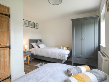 A bedroom with two single beds a grey wardrobe a wooden door and framed pictures on the wall at Bwthyn Y Swnt in Moelfre