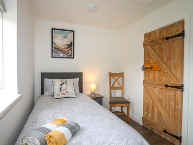 A small bedroom with a single bed a wooden chair a wooden door and a framed picture at Bwthyn Y Swnt in Moelfre