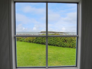 A window view of a green lawn and shrubs with the sea and an island in the background at Bwthyn Y Swnt in Moelfre