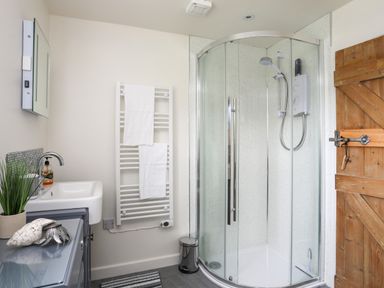 A bathroom with a curved glass shower enclosure a wooden door a white sink and a towel radiator at Bwthyn Y Swnt in Moelfre