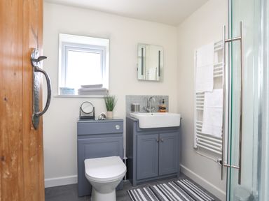 A bathroom with a toilet, sink, mirror, towel rack with towels, and a striped rug at Bwthyn Y Swnt in Moelfre