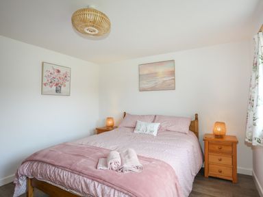 A bedroom with a double bed pink bedding wooden bedside tables lamps and floral curtains at Bwthyn Y Swnt in Moelfre
