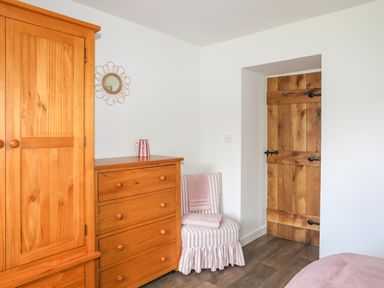 A bedroom corner with wooden wardrobe and chest of drawers striped chair wooden door at Bwthyn Y Swnt in Moelfre
