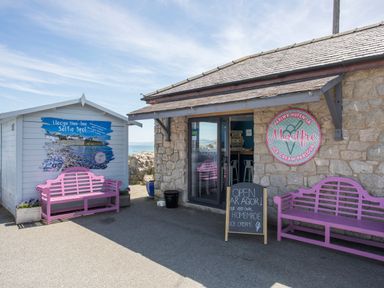 An ice cream parlour with stone walls two pink benches and a chalkboard sign at Bwthyn Y Swnt in Moelfre