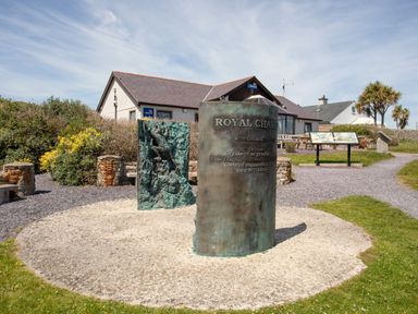 An outdoor memorial with sculptures and information boards near a building with lifeboats signs at Bwthyn Y Swnt in Moelfre