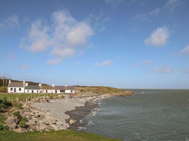 A row of white cottages by a rocky beach with grassy hills and a cloudy sky at Bwthyn Y Swnt in Moelfre