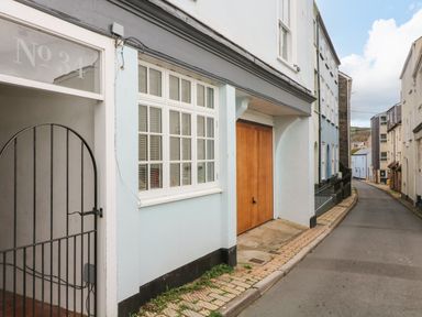 A narrow street with buildings on both sides including a light blue building with a large wooden door and white framed windows at Secret Garden 34C Clarence Street Dartmouth