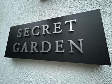 A black sign with white letters saying secret garden on a textured white wall at Secret Garden 34C Clarence Street Dartmouth