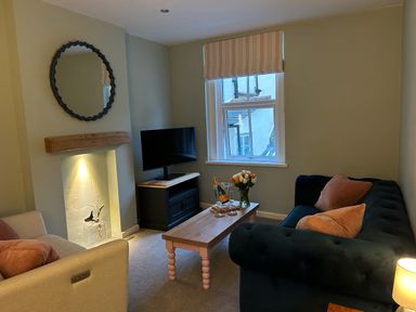 A sitting room with two sofas a coffee table a television a round mirror and a window at Secret Garden 34C Clarence Street in Dartmouth