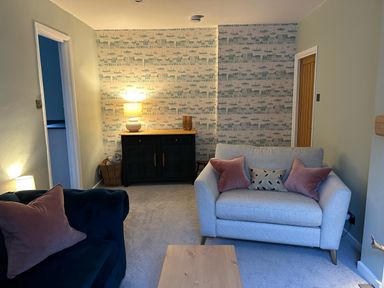 A living room with two sofas a wooden coffee table a lamp on a cabinet and patterned wallpaper at Secret Garden 34C Clarence Street Dartmouth