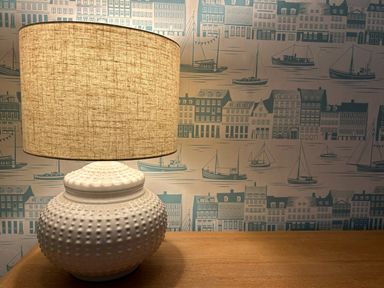 A table lamp with a textured base on a wooden surface and wallpaper with ships and buildings in the background at Secret Garden 34C Clarence Street Dartmouth