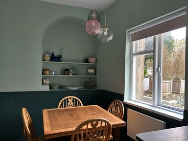 A dining area with a wooden table and four chairs by a window and built in shelves with decorative items at Secret Garden 34C Clarence Street in Dartmouth