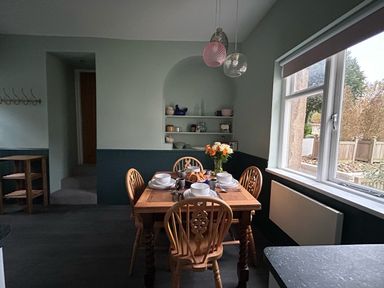 A dining room with a wooden table set for four and a window showing an outdoor garden at Secret Garden 34C Clarence Street Dartmouth