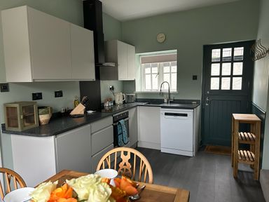 A kitchen with white cabinets black countertop a sink a dishwasher a stove a door and a wooden dining table with flowers at Secret Garden 34C Clarence Street Dartmouth