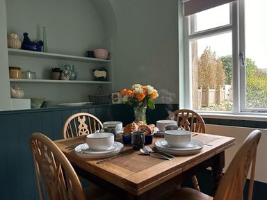A dining room with a wooden table set with bowls plates utensils a vase with flowers and a window at Secret Garden 34C Clarence Street Dartmouth