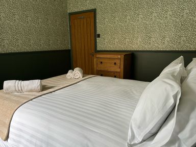 A bedroom with a bed with white sheets and pillows with towels placed on it a wooden chest of drawers and a wooden door at Secret Garden 34C Clarence Street Dartmouth